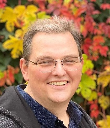 Porträt einer lächelnden Person vor buntem Herbstlaub